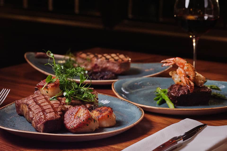Upscale plated dinner with grilled steak, seafood, and garnish on blue plates