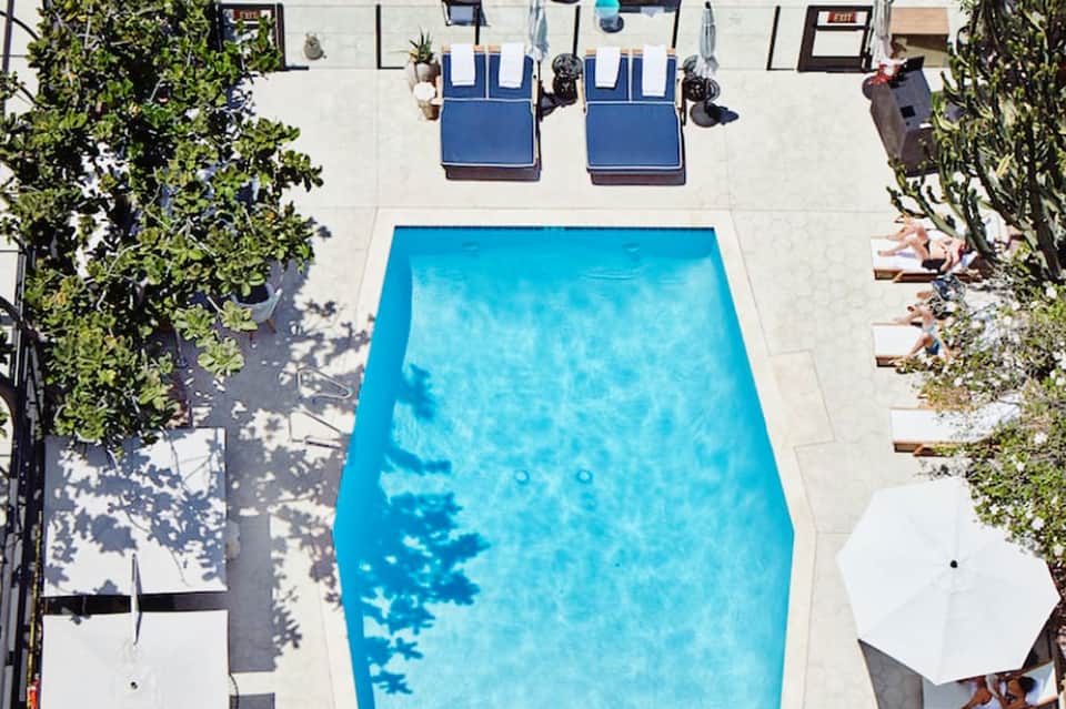 Overhead view of rectangular swimming pool with loungers and shade umbrellas on surrounding patio
