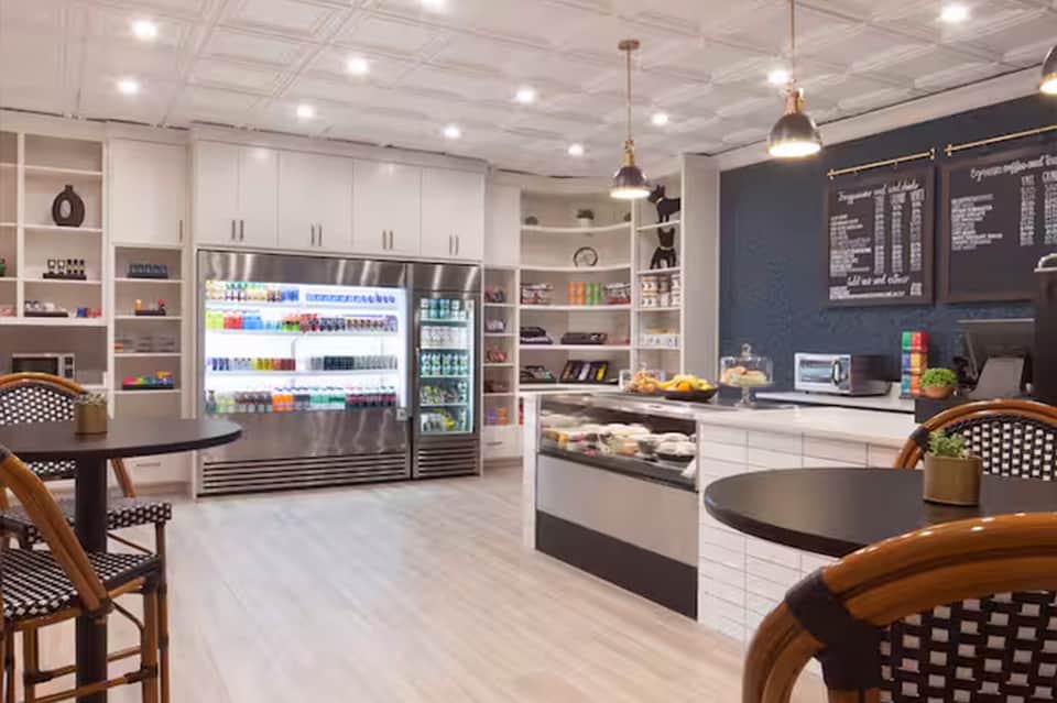 Modern café interior with white cabinetry, refrigerated display cases, black menu boards, and wooden bistro seating