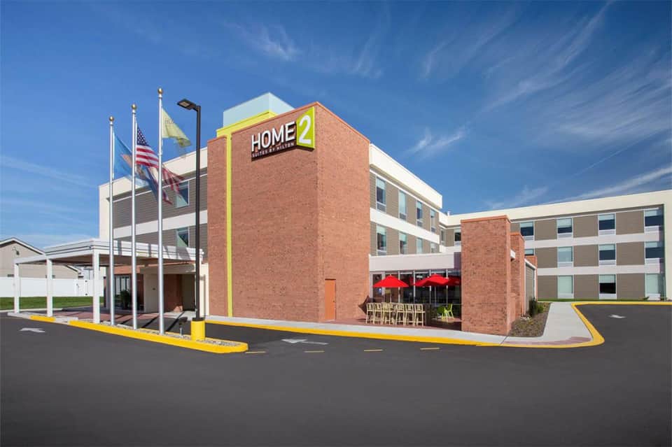 Home2 Suites hotel exterior with brick facade, entrance, and yellow trim under clear blue sky