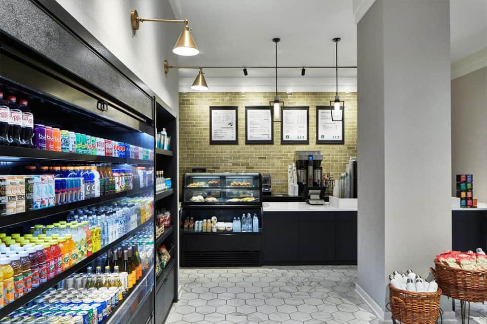Bright café interior with yellow brick wall, refrigerated display case, beverage coolers, pendant lighting, and wooden baskets