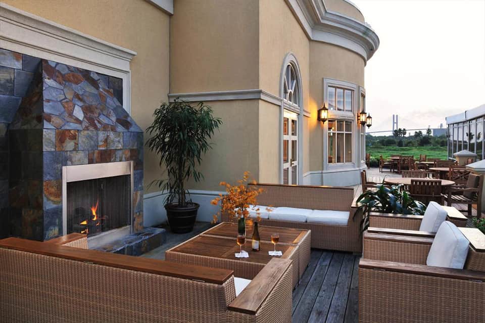 Outdoor patio with fireplace, wicker furniture, white cushions, stone accent wall, and countryside views