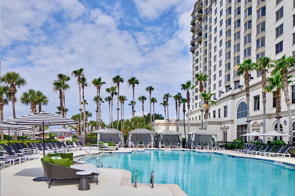 Luxury resort pool with palm trees, loungers, umbrellas, and high-rise building with classical architecture