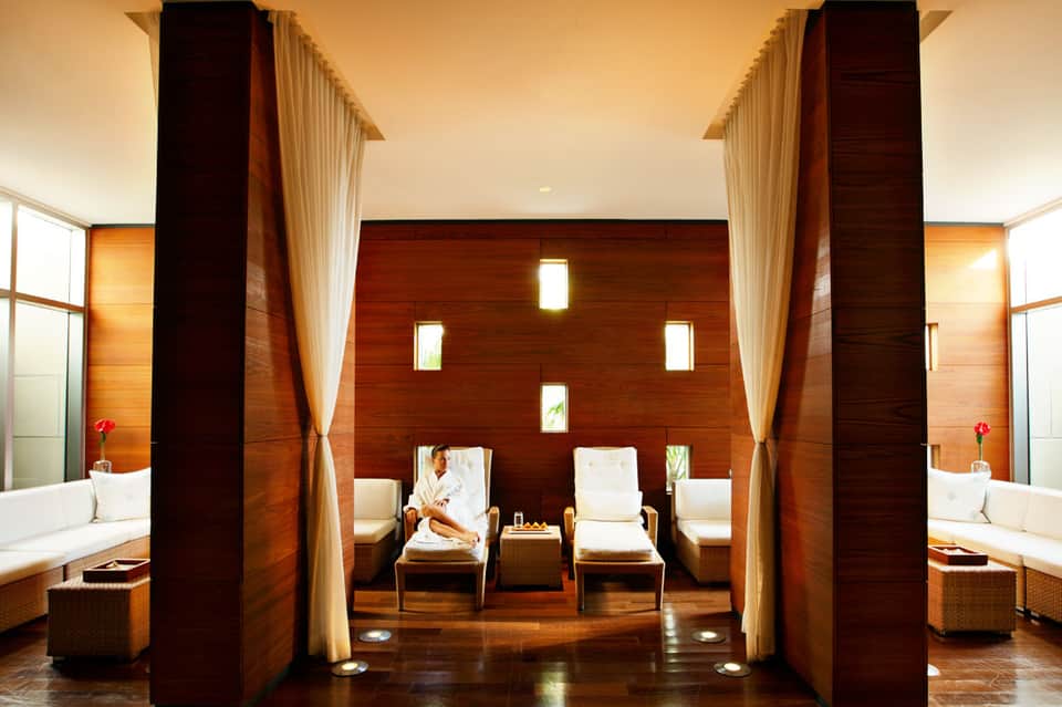 Luxurious spa relaxation area with wooden pillars, cream curtains, lounge chairs, and ambient lighting