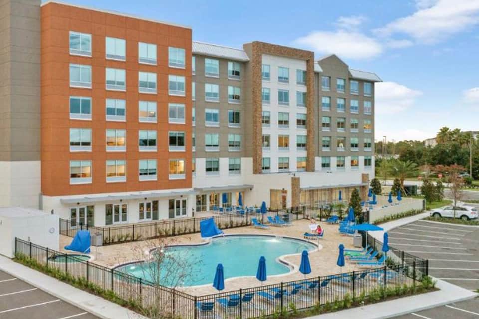Modern multi-story hotel with orange and tan brick facade and outdoor pool with blue umbrellas and playground