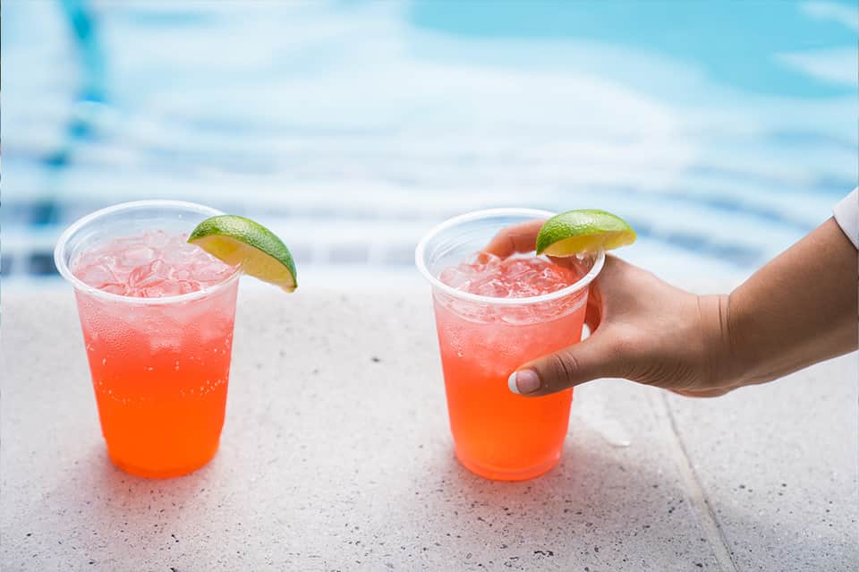 Two coral-colored cocktails with lime garnish by pool overlooking ocean