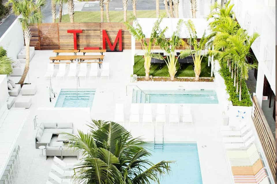 Aerial view of modern resort with palm trees, multiple pools, and red TM signage