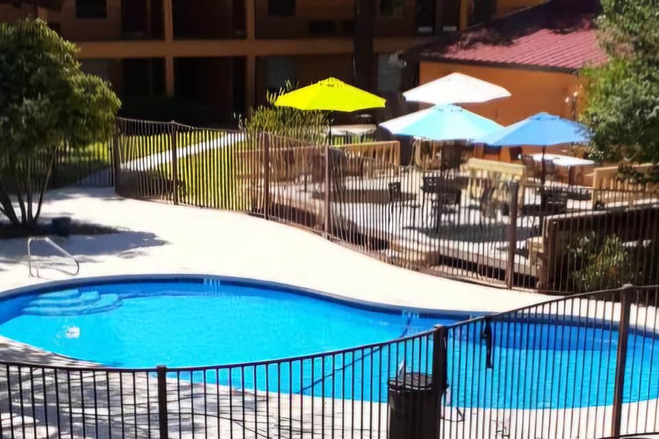 Resort swimming pool with safety fence, colorful umbrellas, and lounge chairs