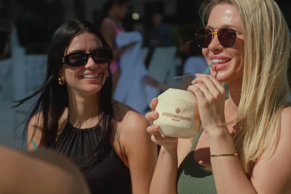 Two women by pool holding branded cups, enjoying beverages at a resort