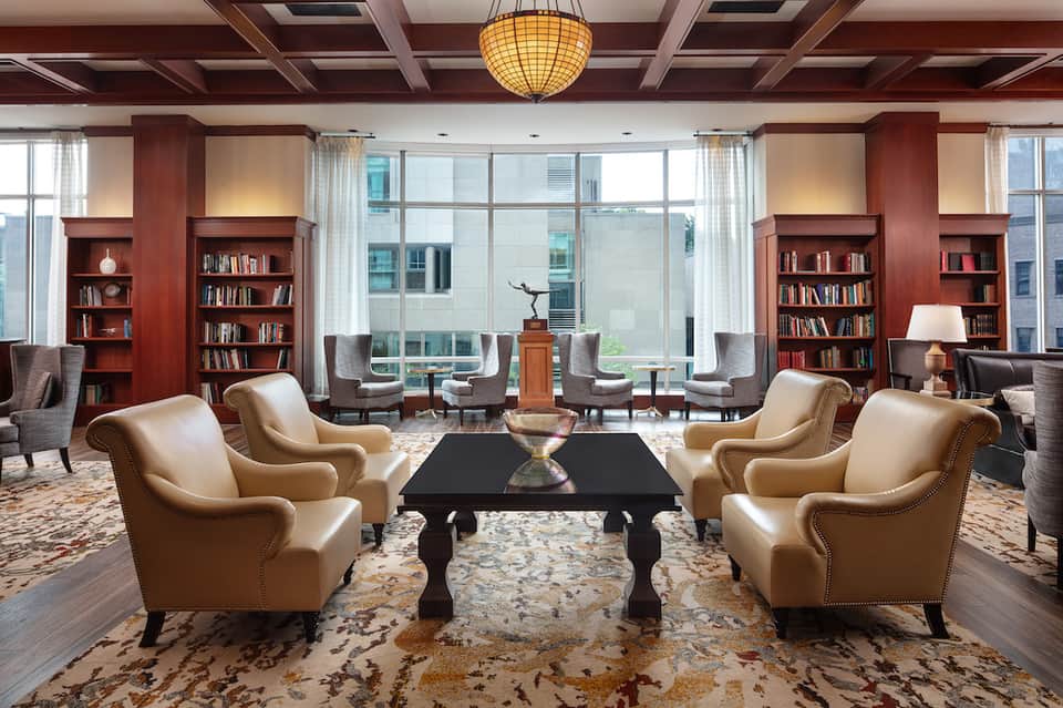 Elegant library lounge with leather chairs, wood bookshelves, coffered ceiling, and city views