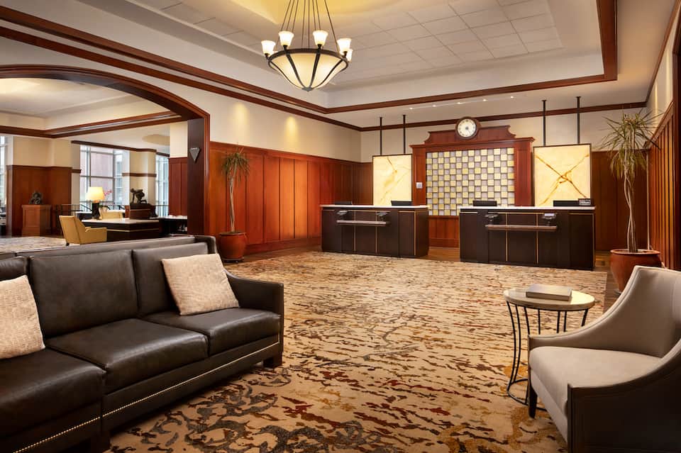 Luxury hotel lobby with dark leather sofa, wooden accents, dual reception desks, and decorative plants