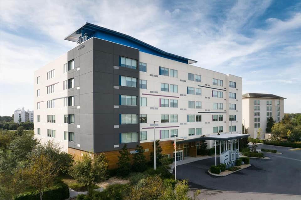 Contemporary hotel exterior with five-story white and dark gray facade, blue roofline accent, and entrance