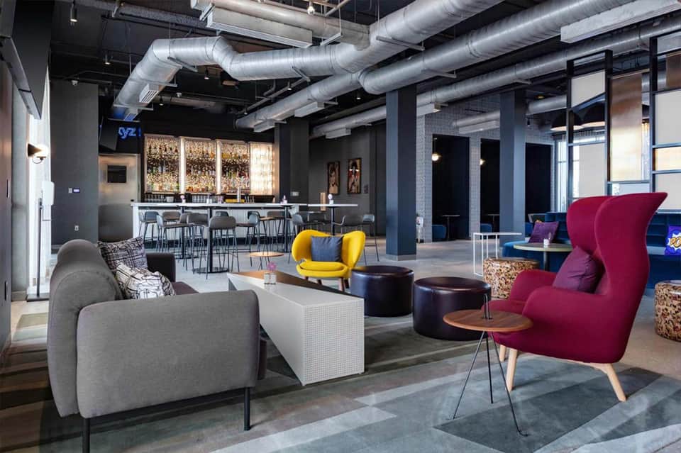 Modern hotel lobby with colorful accent chairs, exposed ductwork, and sophisticated seating areas