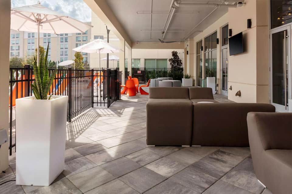 Contemporary rooftop lounge with brown modular seating, white umbrellas, potted plants, and city skyline views