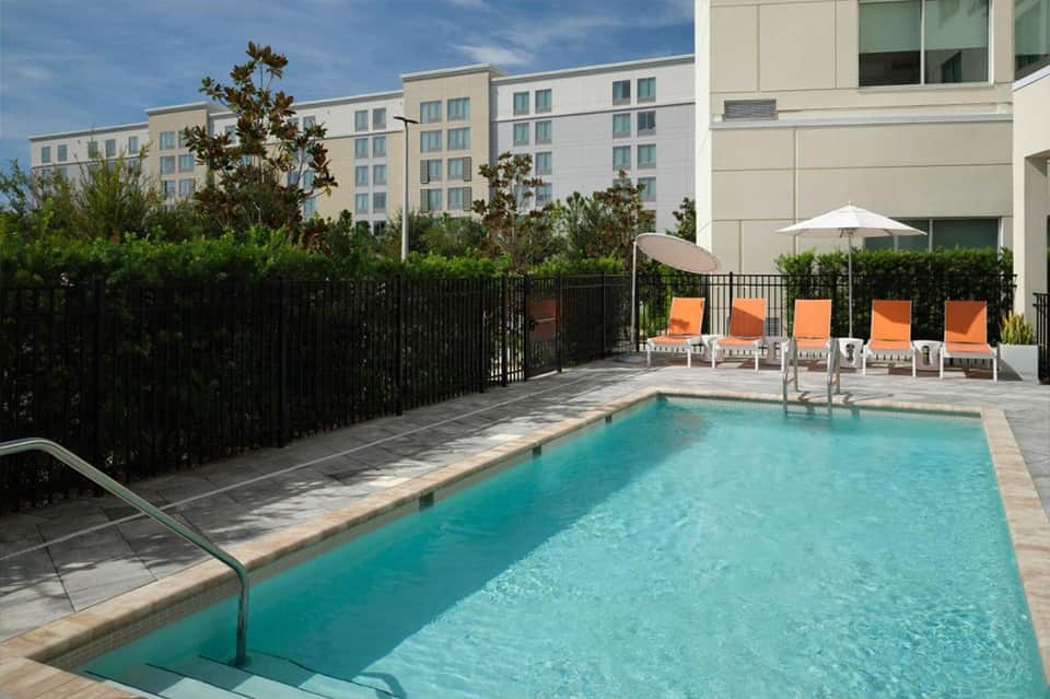 Compact residential pool with turquoise water, orange lounge chairs, and hedge privacy fencing