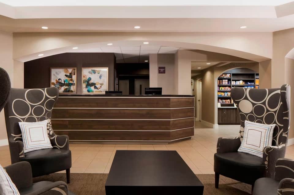 Modern hotel lobby with curved dark wood reception desk, decorative chairs, and contemporary artwork