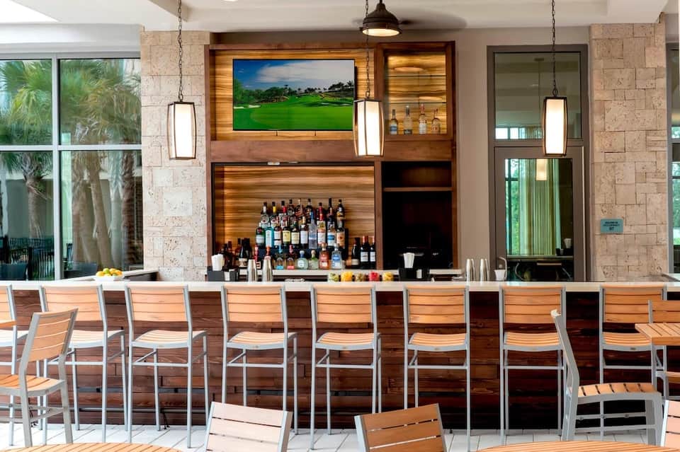 Modern indoor bar with wooden shelving displaying bottles, flat-screen TV, and contemporary bar seating