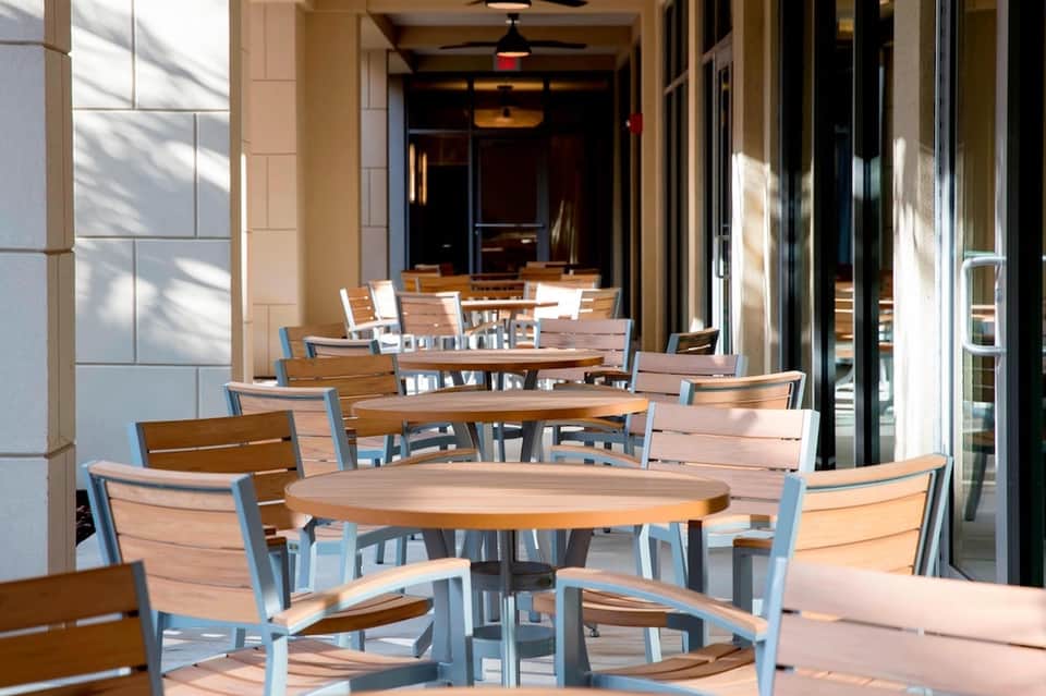 Modern outdoor dining area with wooden tables and blue chairs on a covered terrace