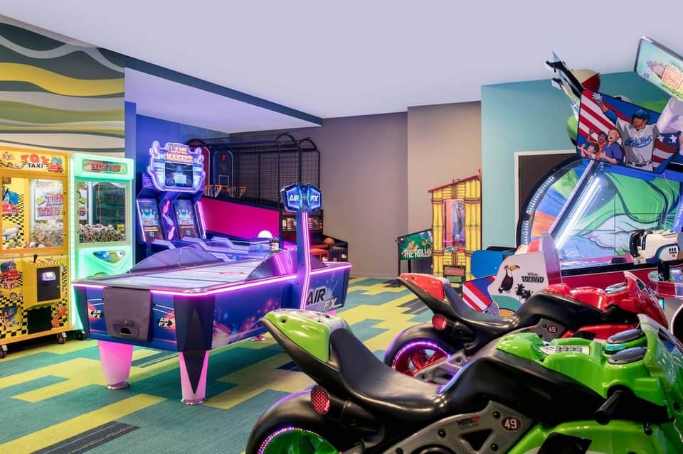 Colorful arcade game room with neon-lit racing simulators and air hockey table