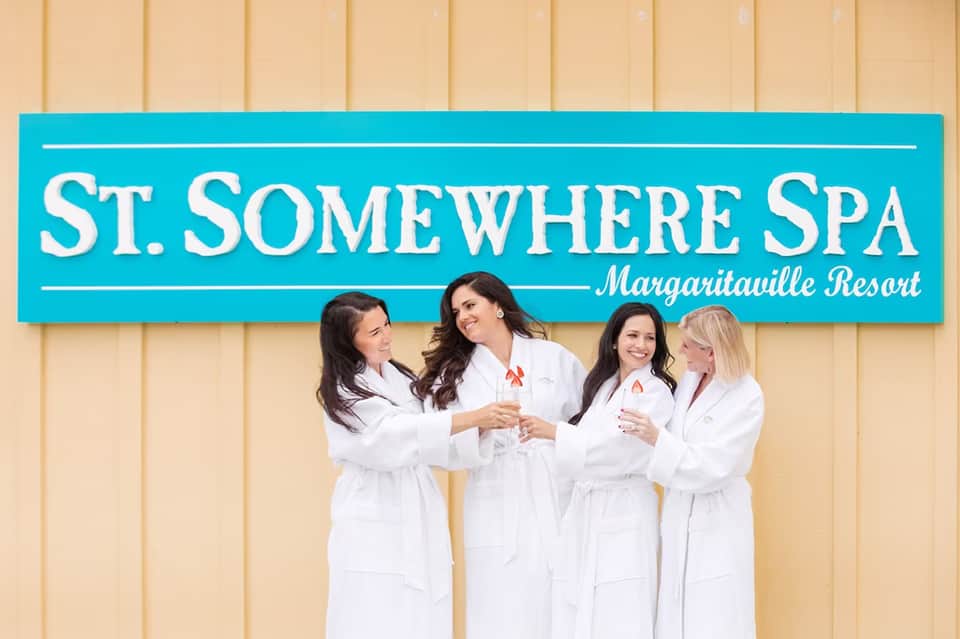 Four spa staff members in white bathrobes smiling under St. Somewhere Spa Margaritaville Resort signage