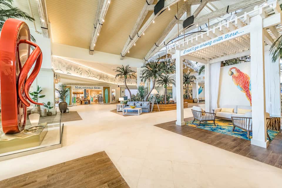Bright mall interior with tropical plants, red sculptural art, and modern retail storefronts