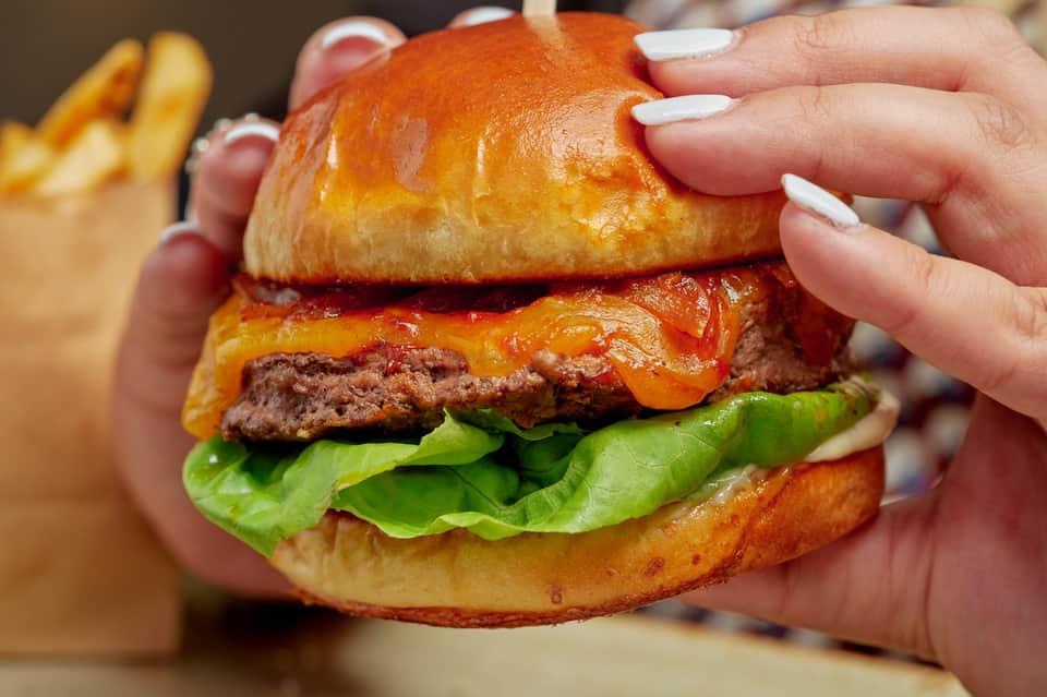 Gourmet cheeseburger with melted orange cheese, lettuce, and brioche bun held in hands