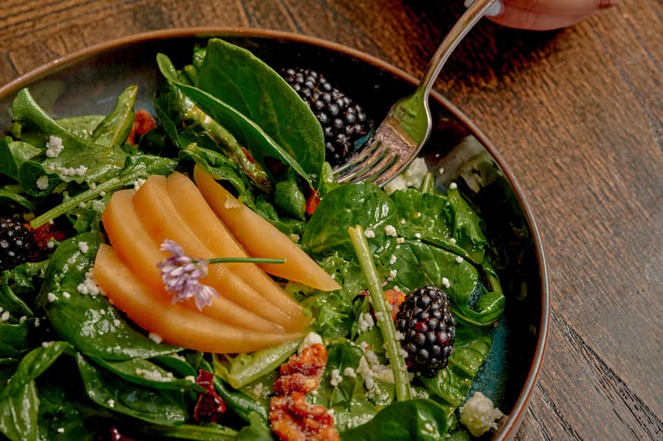 Gourmet salad with fresh greens, berries, and edible flowers on dark plate