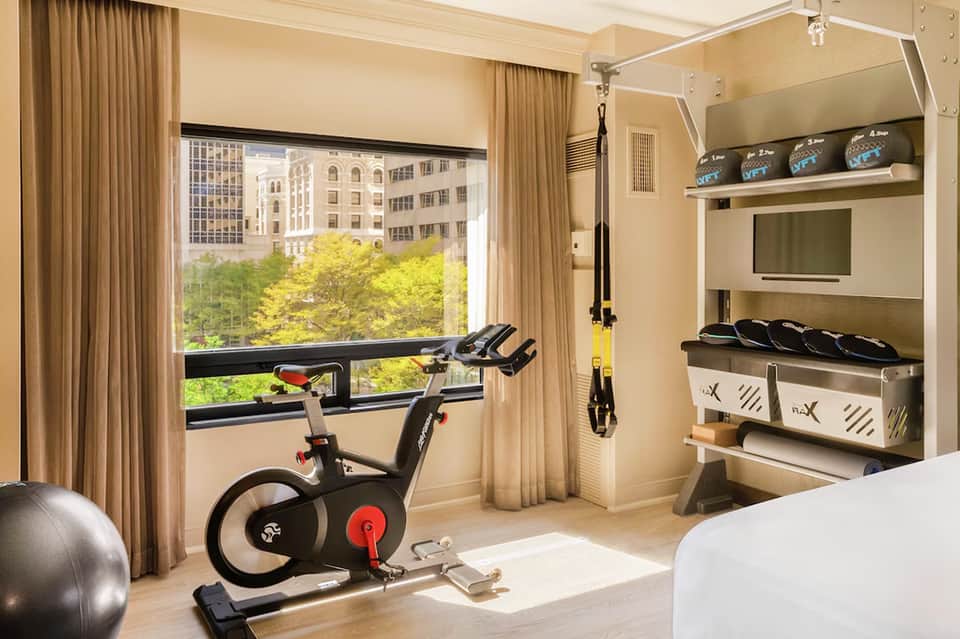 Modern hotel fitness room with exercise bike, window view of cityscape, and equipment storage