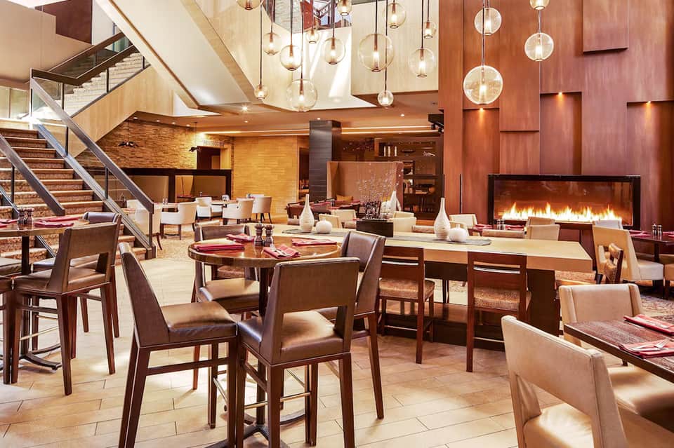 Upscale restaurant interior with modern pendant lighting, fireplace, stairs, and elegant dining setup