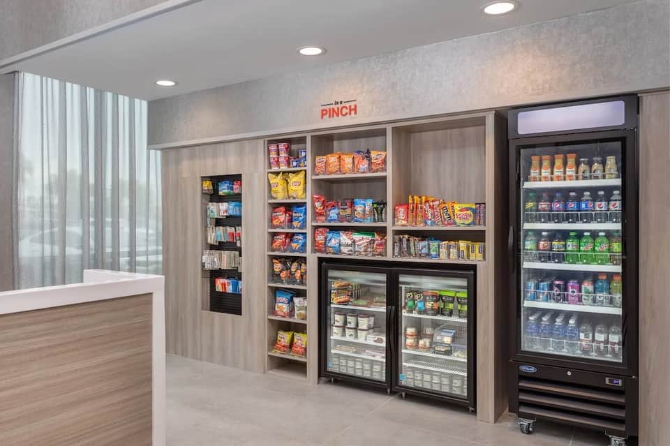 Hotel snack shop interior with wooden cabinetry, refrigerated beverage case, and shelves stocked with packaged snacks