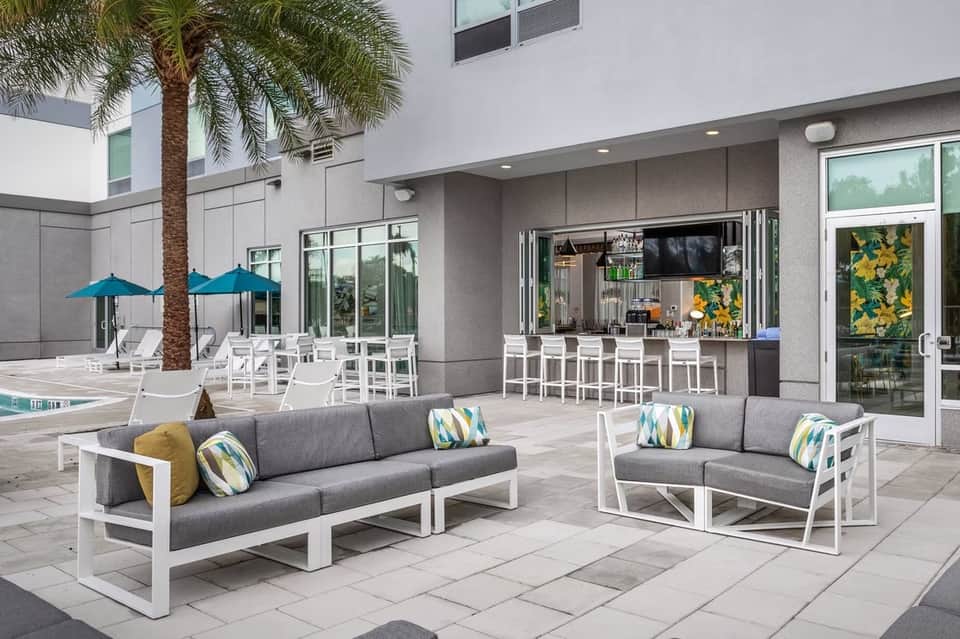 Modern courtyard with lounge seating, blue umbrellas, palm tree, tiki bar, and fireplace seating area