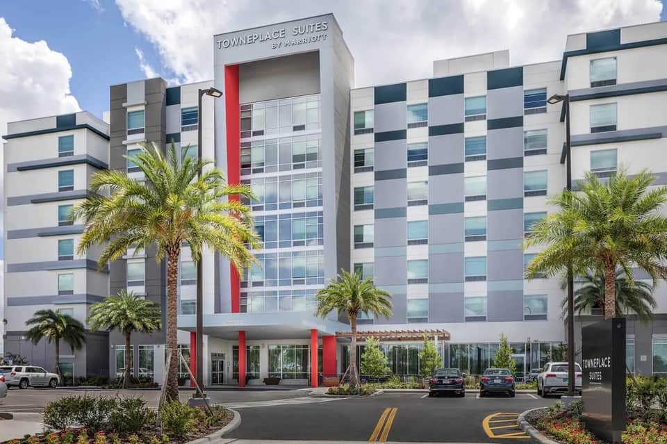 TownePlace Suites hotel exterior with modern white and blue checkered facade, red accents, and palm trees