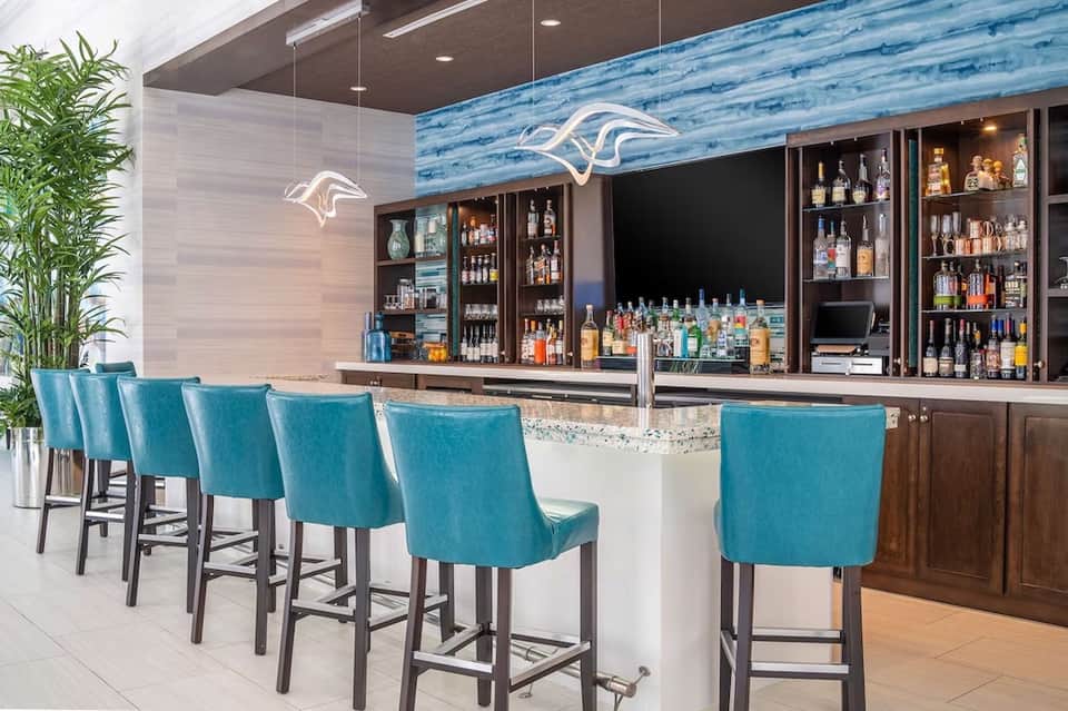 Modern bar with turquoise upholstered seating, neon dolphin sign, and fully stocked liquor shelves