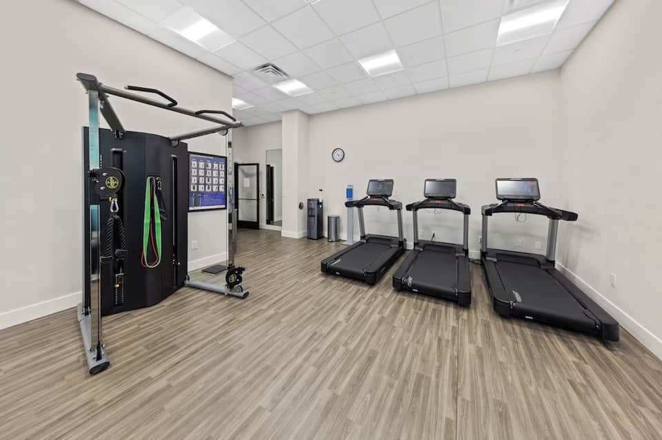 Fitness center with treadmills, exercise equipment, and a cable machine on wooden flooring