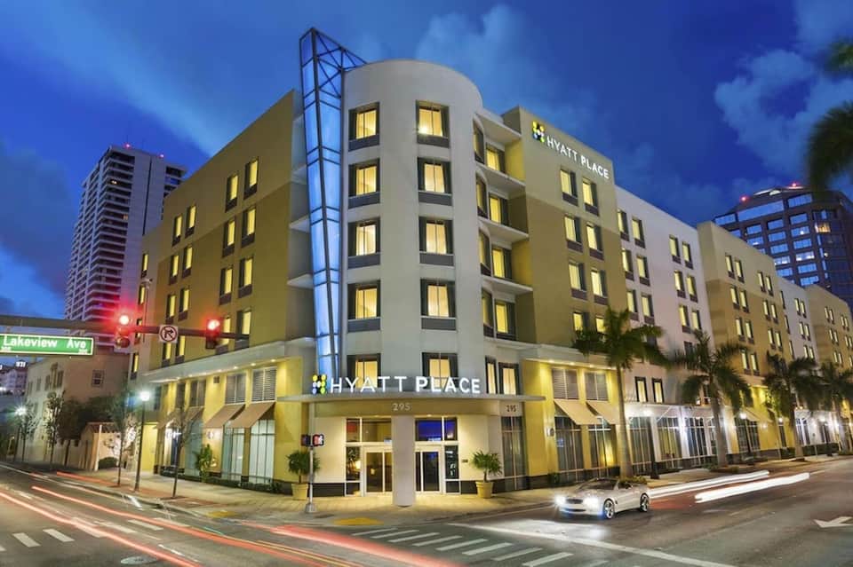 Hyatt Place hotel exterior at dusk with illuminated yellow facade and palm trees