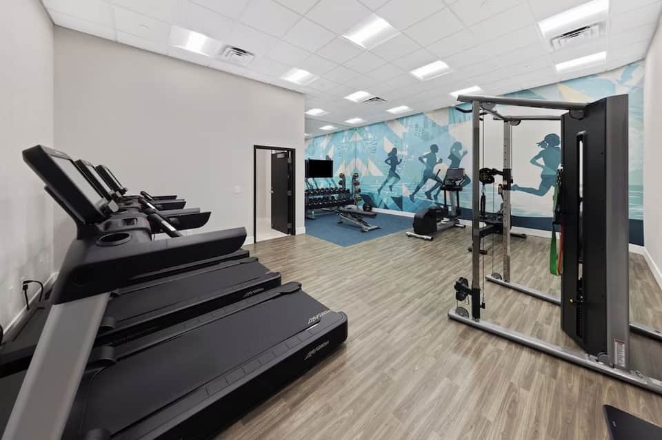 Well-equipped fitness center with treadmills, exercise machines, motivational wall mural, and light wood flooring