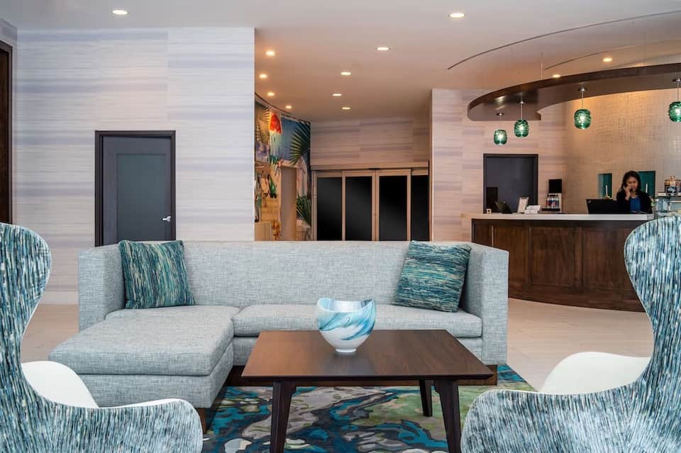 Modern hotel lobby with gray sectional sofa, teal accents, and curved reception desk