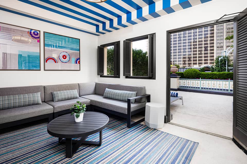 Modern lounge area with striped ceiling, gray seating, blue accent rug, and balcony access