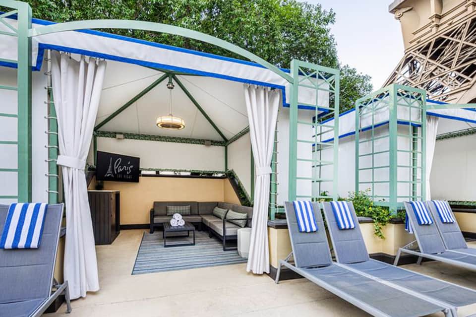 Luxurious cabana with white curtains, blue striped loungers, and seating area