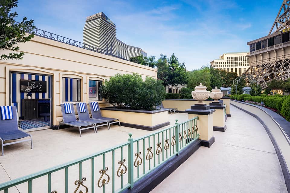 Elegant rooftop terrace with blue and white striped lounge chairs, potted plants, and city skyline views