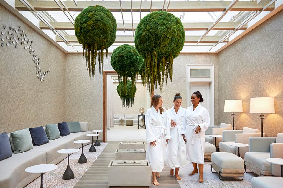 Spa relaxation room with hanging moss balls, fireplace, lounge seating, and three guests in white robes
