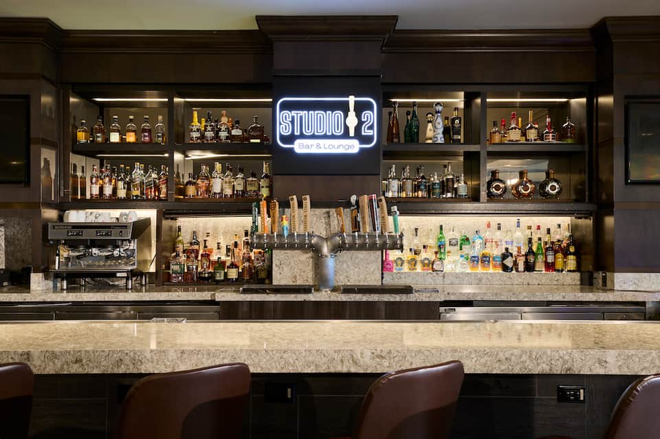 Studio 2 Bar & Lounge interior with neon sign, extensive liquor bottles, and marble counter