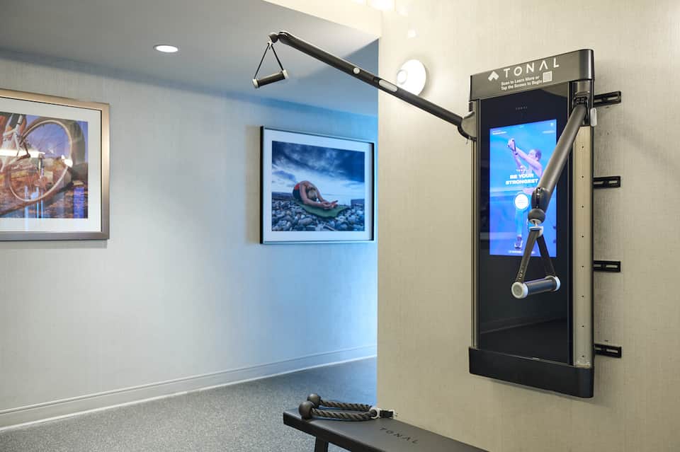 Modern fitness room with blue accent wall, framed artwork, and interactive exercise machine with screen display