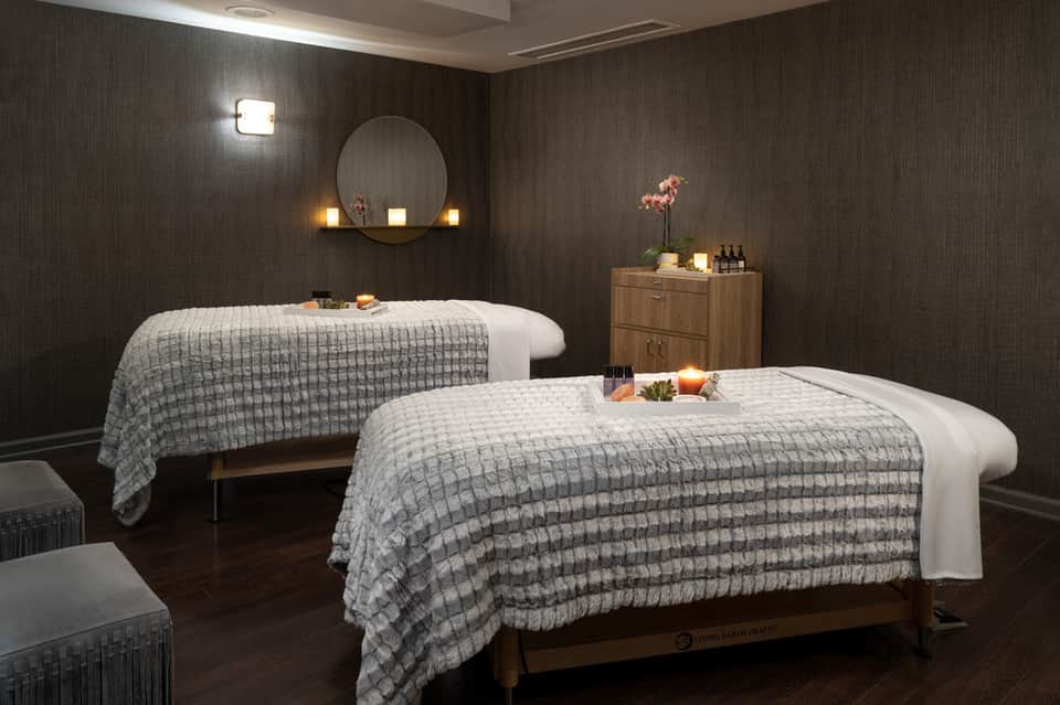 Spa treatment room with two massage tables, dark textured walls, and ambient lighting