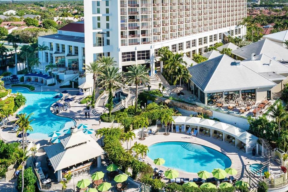 Aerial view of resort with multiple pools, palm trees, and high-rise hotel buildings