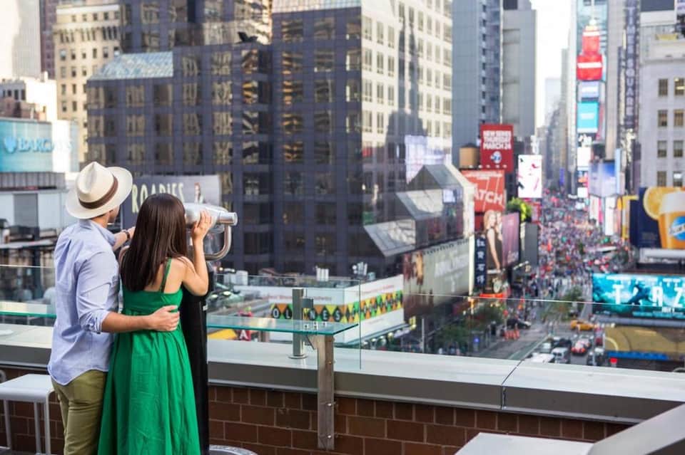 Couple viewing cityscape from observation deck with telescope overlooking Times Square