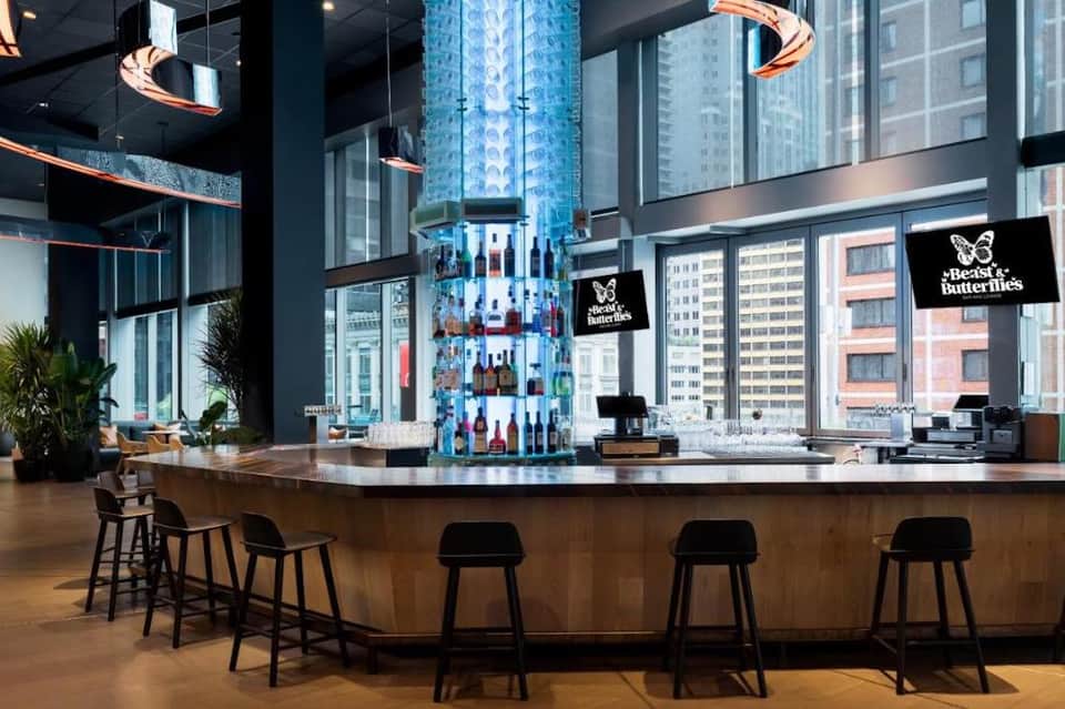 Modern hotel bar with tall bottle display, copper lighting fixtures, and city skyline views