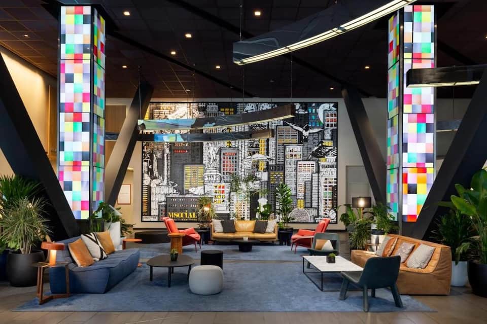 Modern hotel lobby with colorful pixelated columns, city skyline mural, and contemporary furniture arrangement