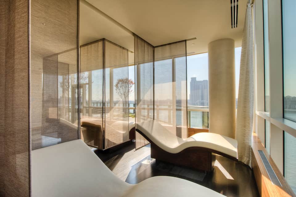 Spa relaxation room with lounge chairs and floor-to-ceiling windows overlooking cityscape