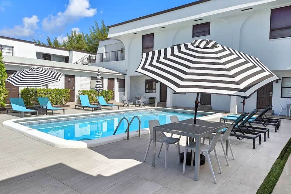 Outdoor pool area with striped black and white umbrellas, modern white buildings, and lounge seating